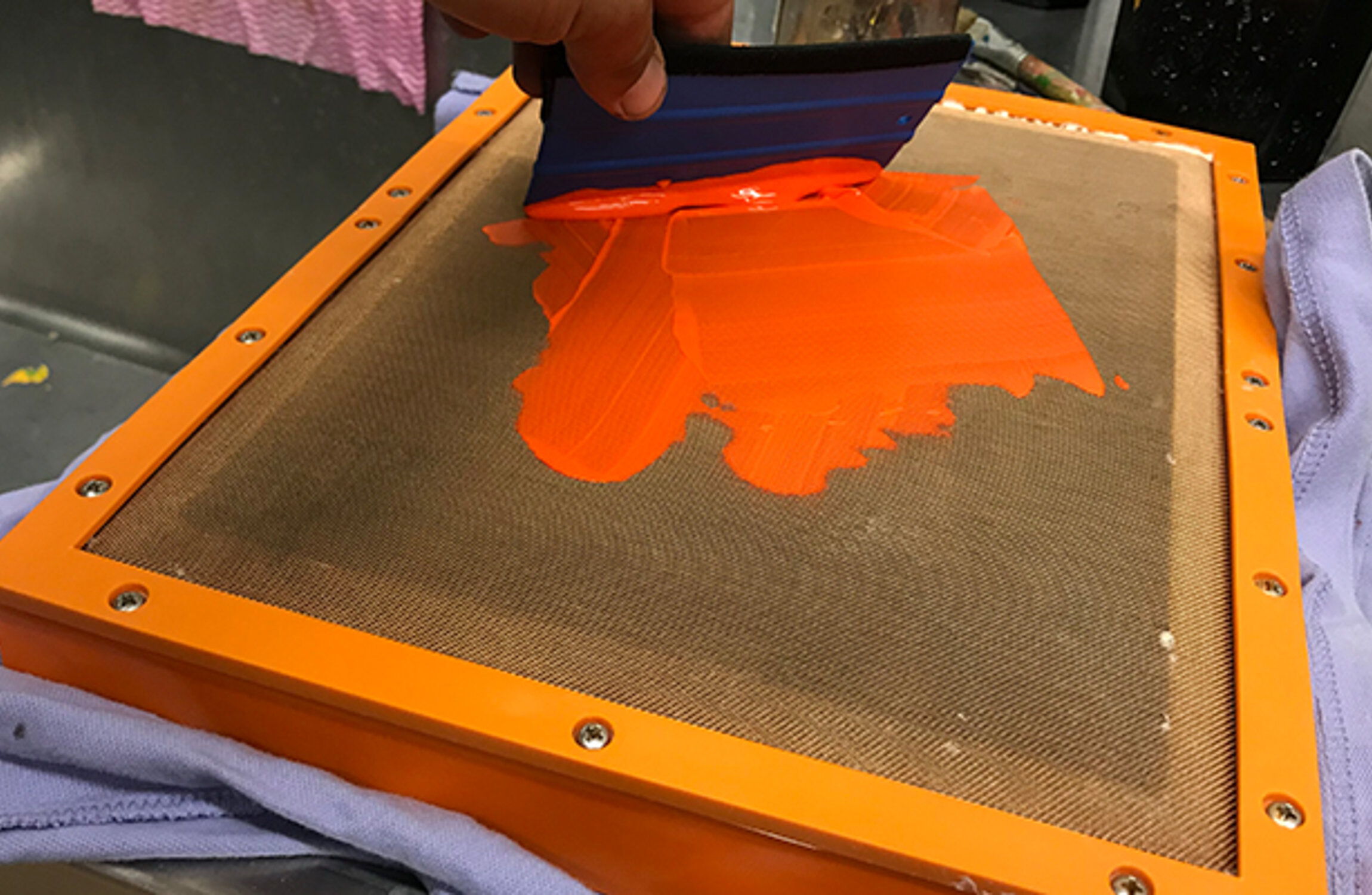 Orangene Farbe wird mit einem Spachtel auf einem Siebdruckrahmen verteilt