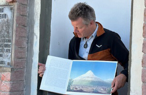 Peter Korneffel hält ein offenes Buch in der Hand mit einer Zeichnung eines schneebedeckten Berggipfels.