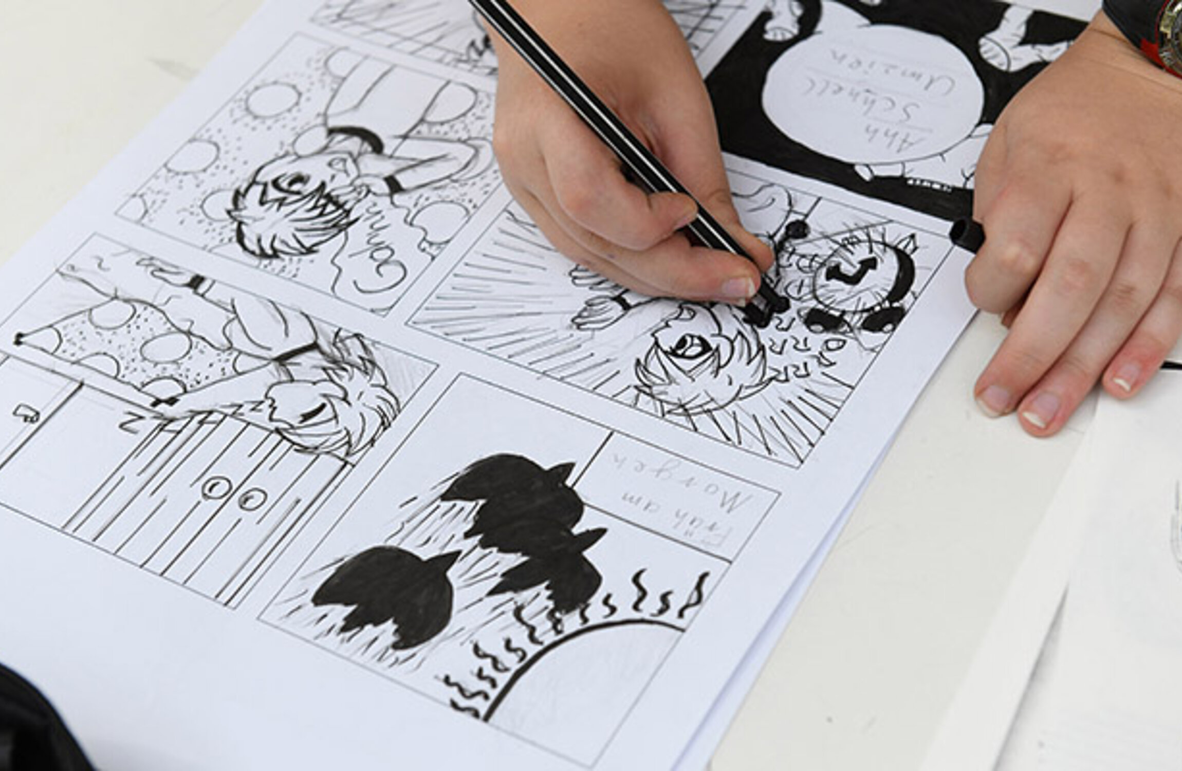 Detailansicht einer Hand, die auf einem Papier mit vielen kleinen, schwarz-weißen Comic-Bildern zeichnet