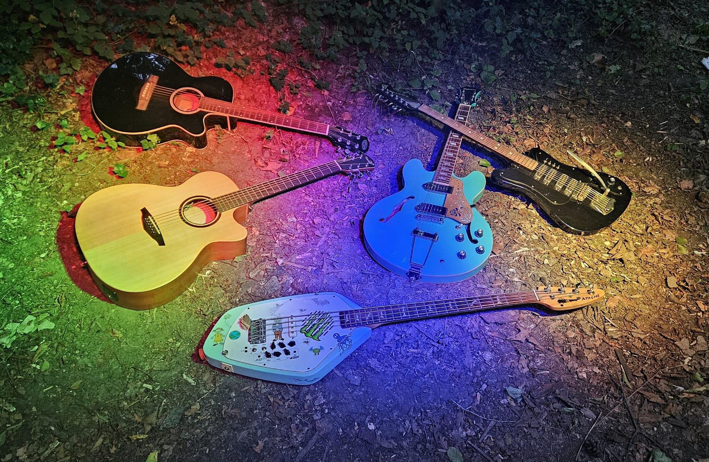 Verschiedene Gitarren liegen in einem Kreis auf dem Boden in bunten Lichtkegeln.