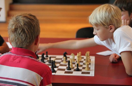 Ein Junge greift mit ausgestrecktem Arm nach einer Figur auf einem Schachspielfeld