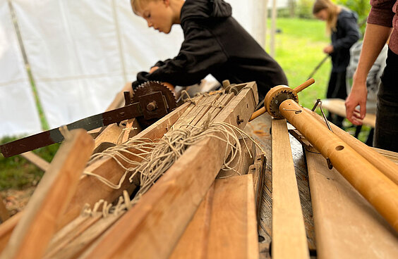 Holzlatten liegen auf einem Tisch und Kinder bearbeiten das Holz