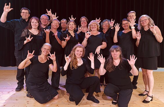 Foto vom Chor Singende Hände. Die Chormitglieder sind in schwarz gekleidet und halten die Hände in die Luft.