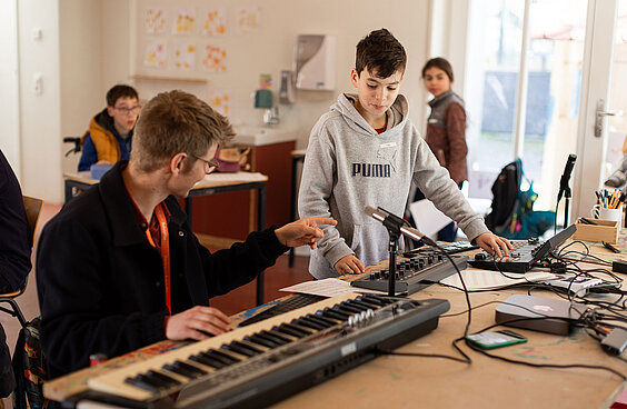Kinder stehen vor einem Piano und Mischpult und mixer einen Song