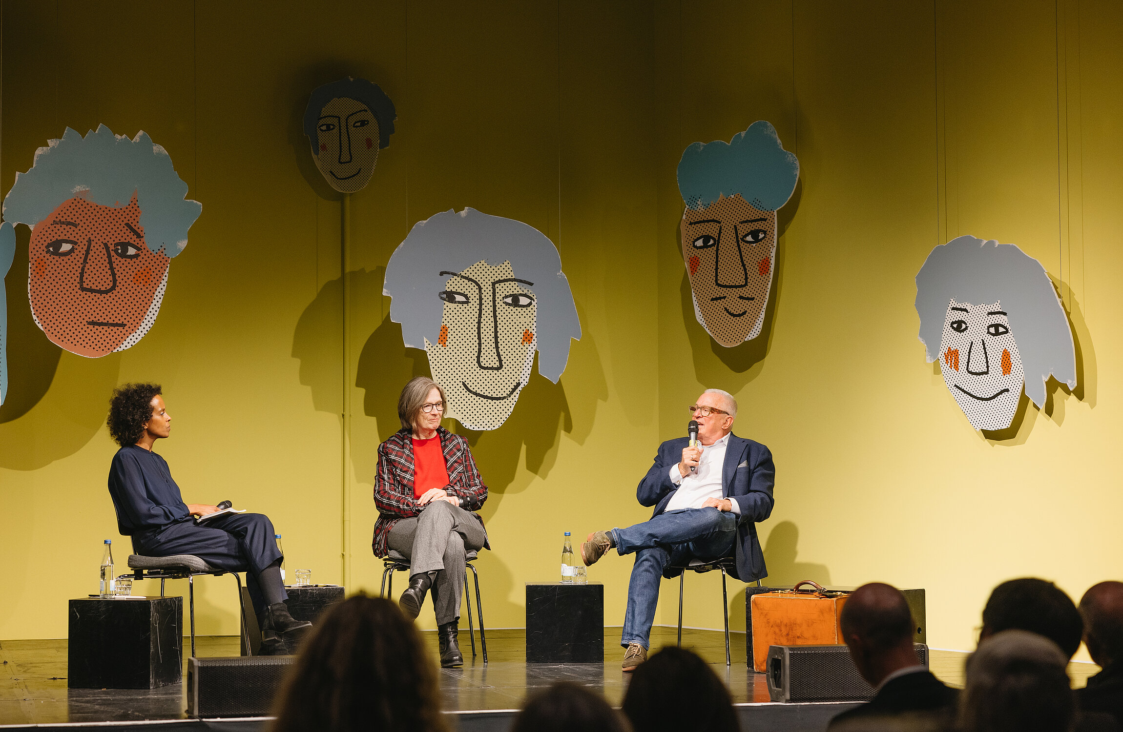 Theresia Volk, Thomas Sattelberger und Boussa Thiam sitzen auf der Werkraum-Bühne vor gelbem Hintergrund.