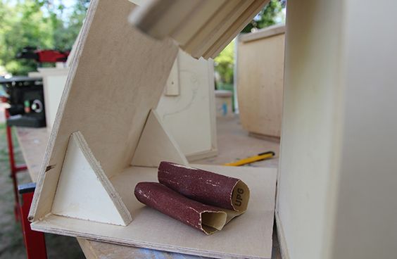 Ein zusammengerolltes Stück Schleifpapier liegt auf einem halbfertigen, kleinen Holzhäuschen