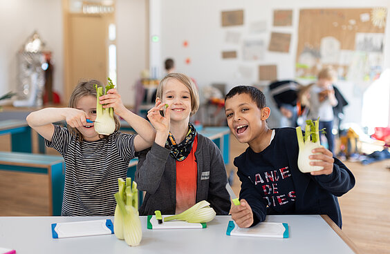 Kinder halten Kohlrabi vor sich und bereiten ihn zu
