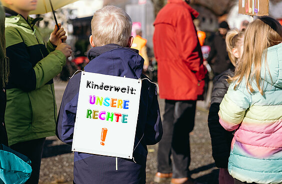 Kind von hinten mit Schild auf dem Rücken auf einer Demo