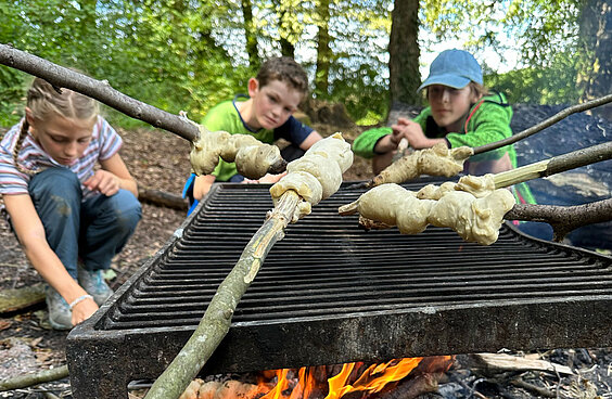 Kinder halten Stockbrot über ein Lagerfeuer