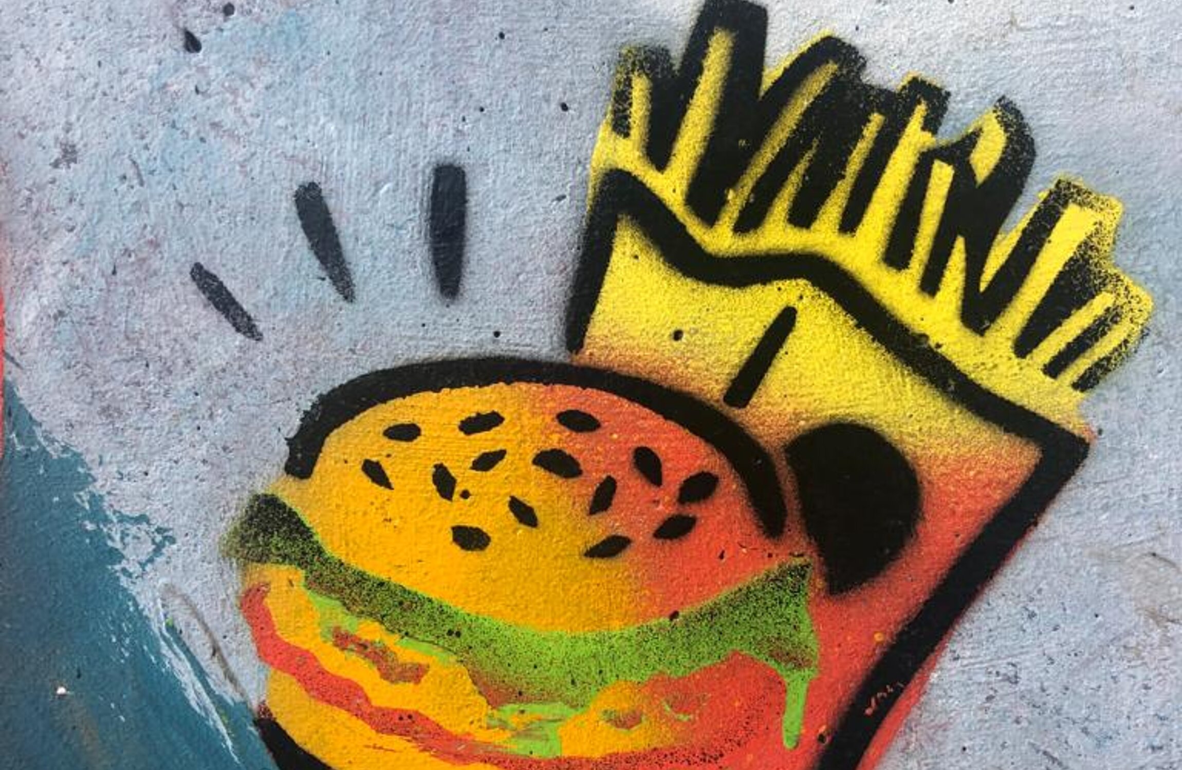 Ein Burger mit einer Tüte Pommes im Hintergrund auf eine Betonfläche gesprüht