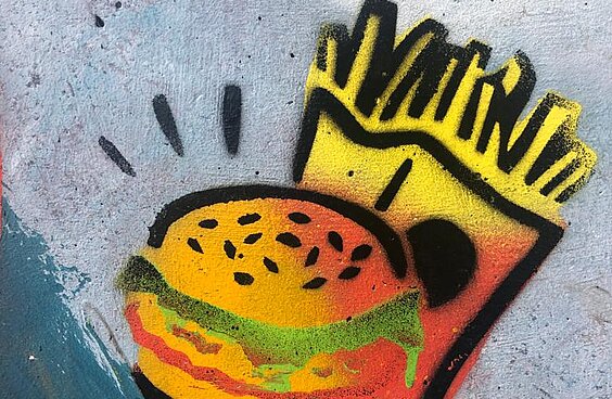 Ein Burger mit einer Tüte Pommes im Hintergrund auf eine Betonfläche gesprüht