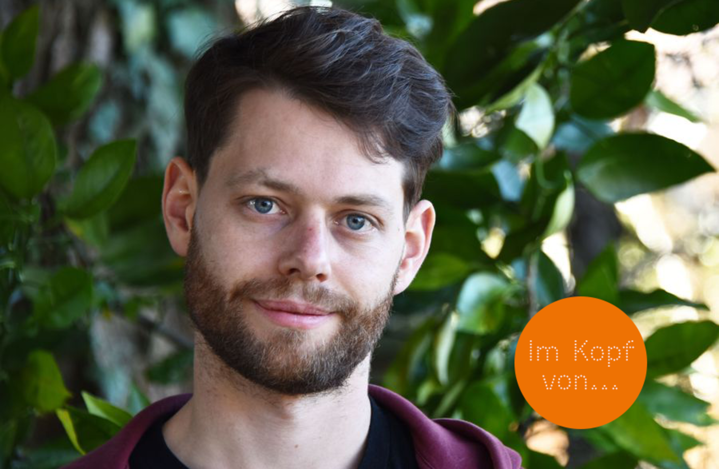 Porträtfoto von Milo Probst vor dichtem Hintergrund aus grünen Blättern. 